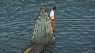 Fisherman lowering his trap from a dugout canoe